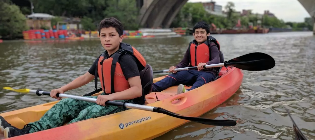 Students kayaking on a calm river during an outdoor adventure learning activity.