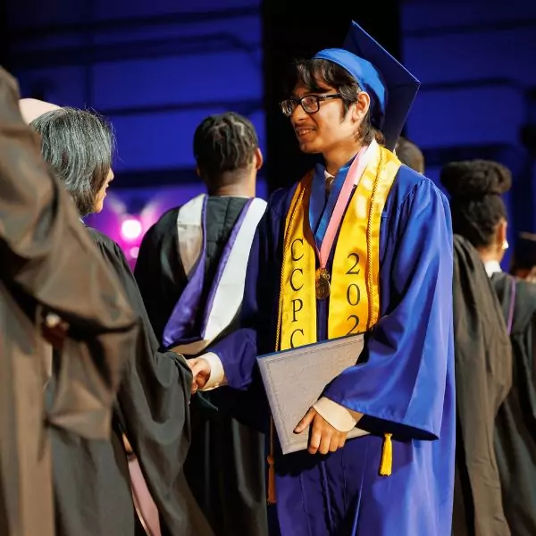 A graduate shakes hands with a faculty member during a 2024 graduation ceremony, holding a diploma.